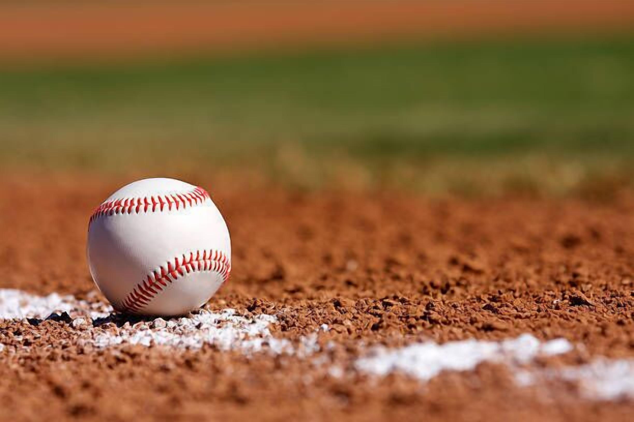 A baseball on a dirt infield with a blurred green background.