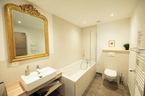 Un baño moderno con un espejo grande, una bañera, un inodoro y una ducha.