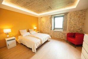 Un dormitorio con cama, lámparas de noche, una silla roja, una pared de piedra y una ventana.