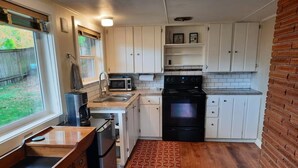 A compact kitchen with white cabinets, a microwave, a stove, and a refrigerator. - Private & Spacious Daylight Basement Apartment with Kitchen (Seattle)