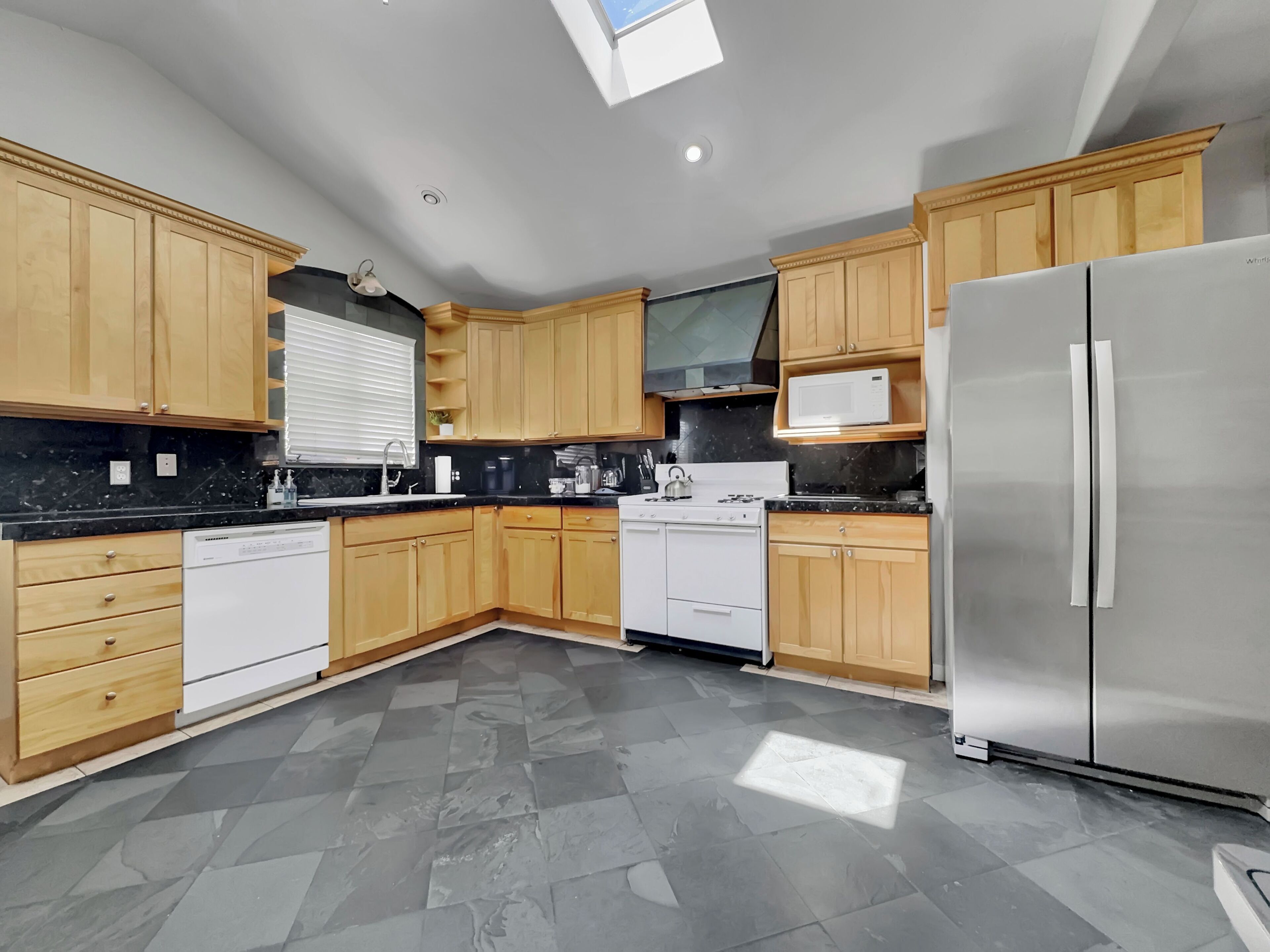 A modern kitchen with wooden cabinets, a stainless steel refrigerator, a dishwasher, and a gas stove.
