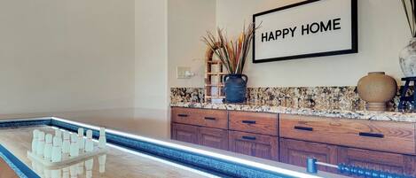 A modern kitchen with a bowling alley setup, wooden cabinets, granite countertop, and a 'HAPPY HOME' sign on the wall.