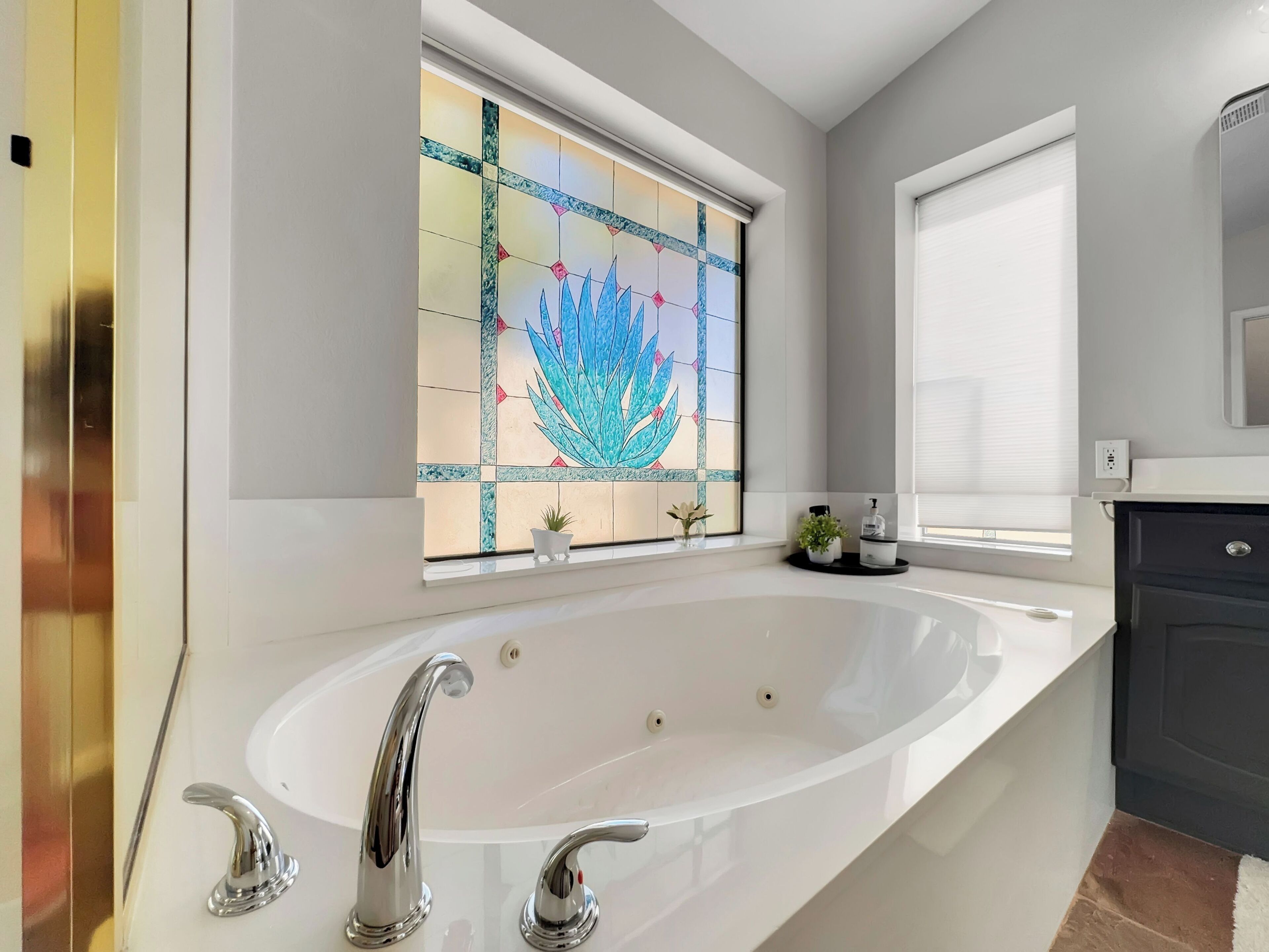 Une salle de bain moderne avec une grande baignoire sur pieds, un vitrail décoratif et une petite plante en pot posée sur le rebord de la fenêtre.