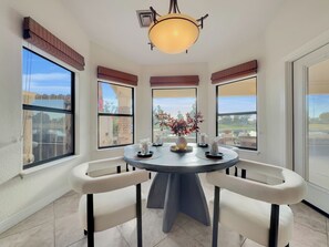 A dining area with a round table, two chairs, a hanging light fixture, and large windows offering views of the outside. - Oleander Ocotillo Chandler Complex (Chandler)