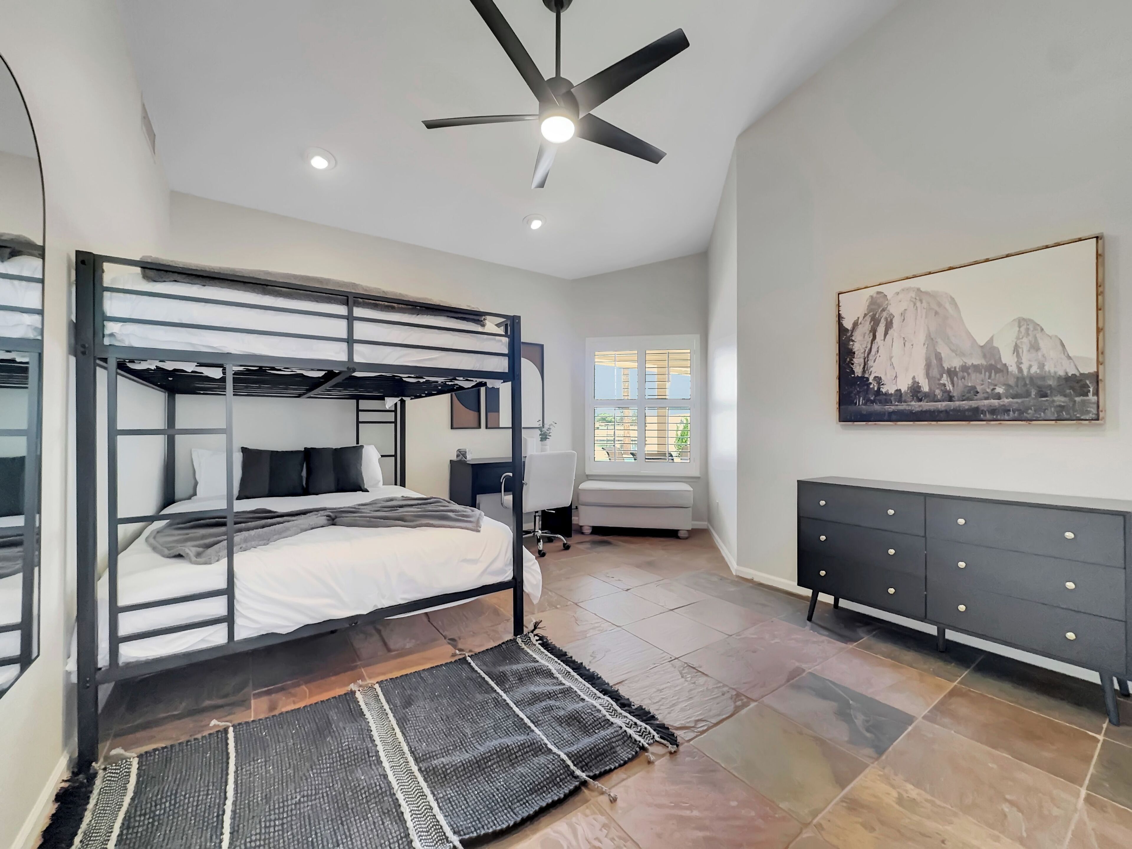 Une chambre moderne équipée de lits superposés, d’un bureau, d’une chaise, d’une commode et d’un ventilateur de plafond.