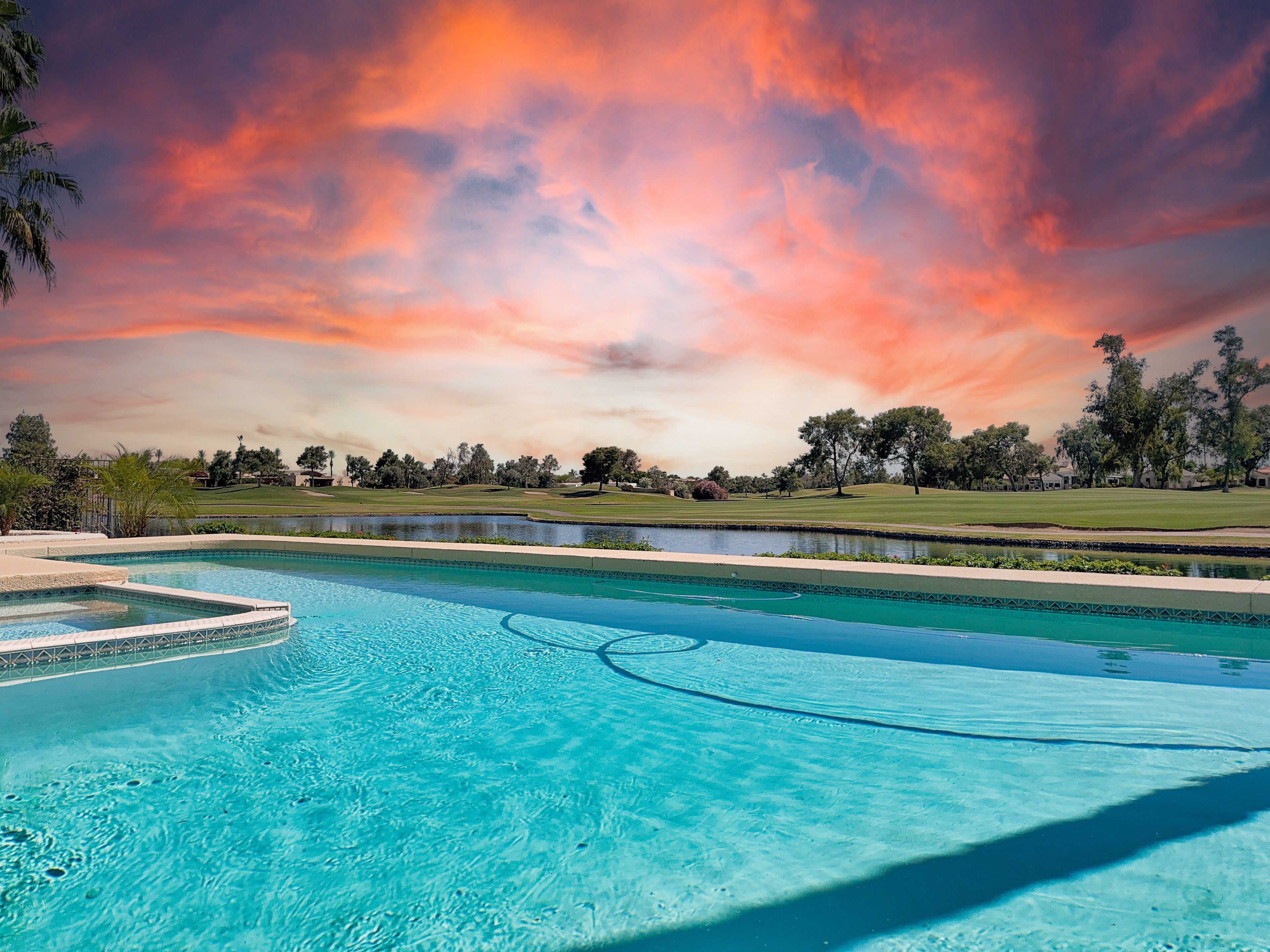 A swimming pool with clear blue water, surrounded by a landscaped area with trees and a golf course in the background.
