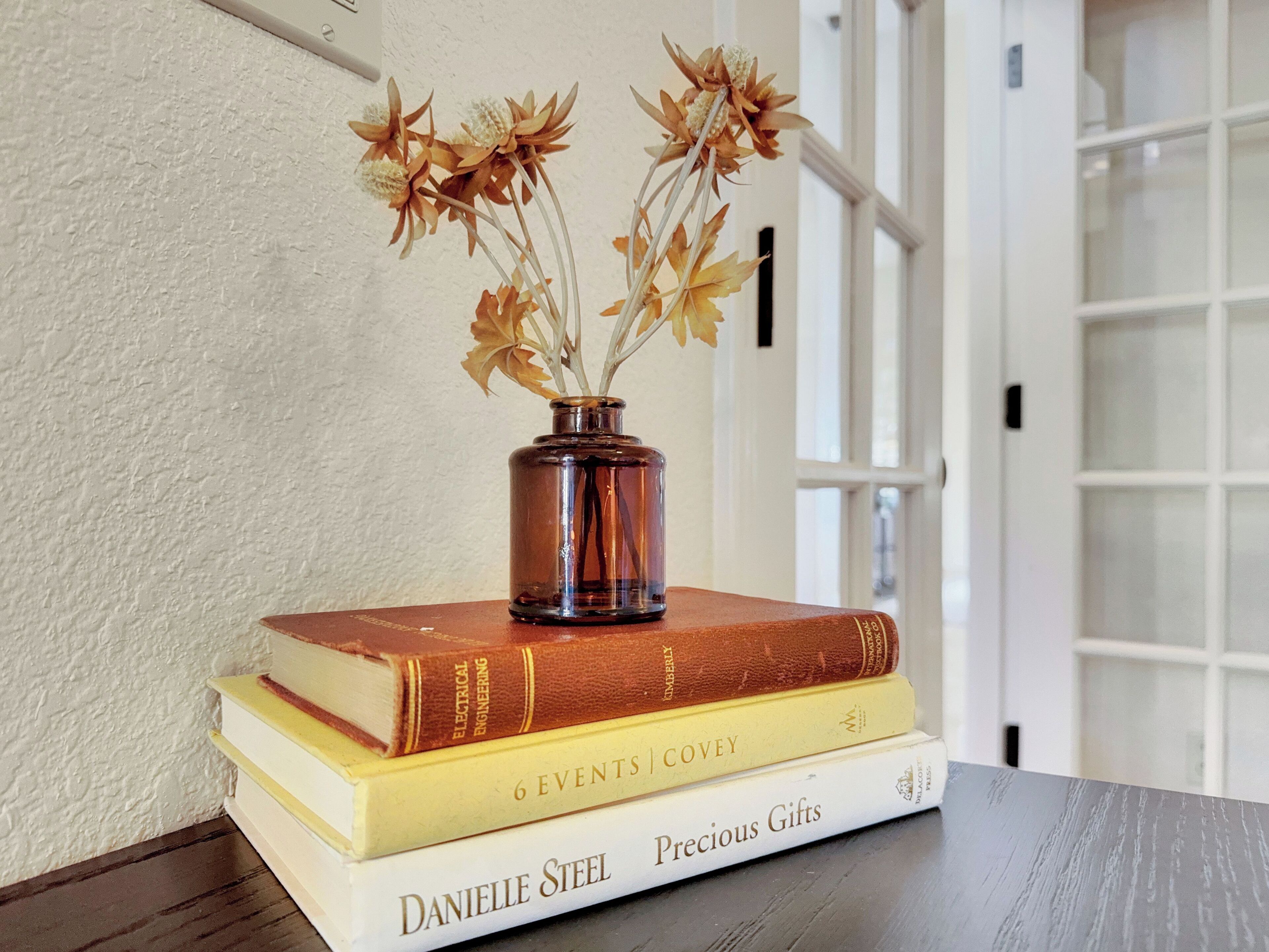 A stack of books with a vase of dried flowers on top.
