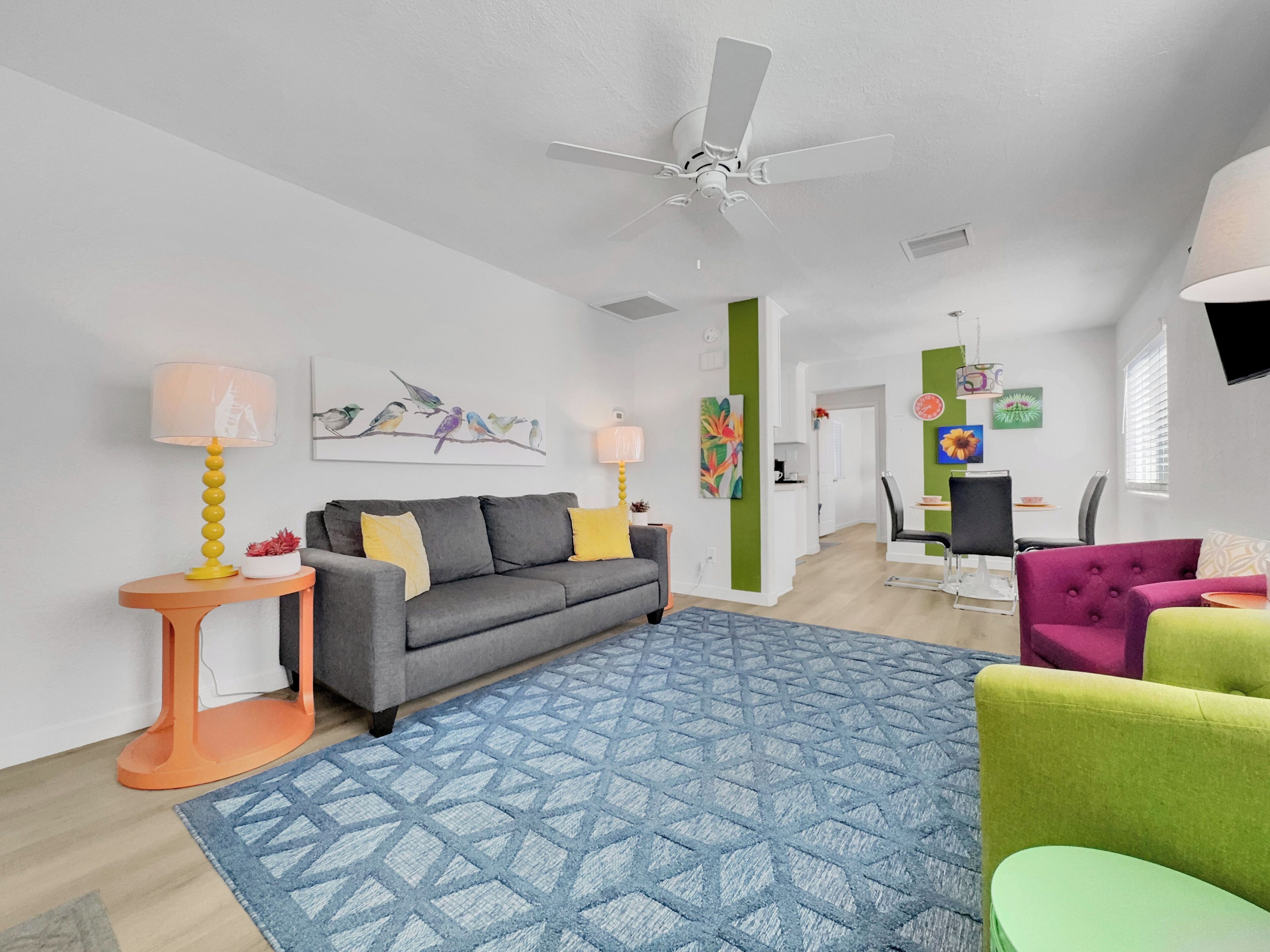 Un salon moderne avec un canapé gris, un tapis à motifs bleus, un ventilateur de plafond et un coin repas comprenant une table et des chaises.