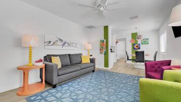 Un salon moderne avec un canapé gris, un tapis à motifs bleus, un ventilateur de plafond et un coin repas comprenant une table et des chaises.