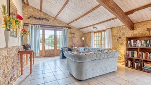 A rustic room with a stone wall, a large cushioned sofa, a wooden bookshelf, and a stone floor. - La Bergerie – Charming House with Shared Pool (Le Buisson-de-Cadouin)