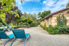 A stone building with a gravel driveway, outdoor seating with chairs, and lush greenery.