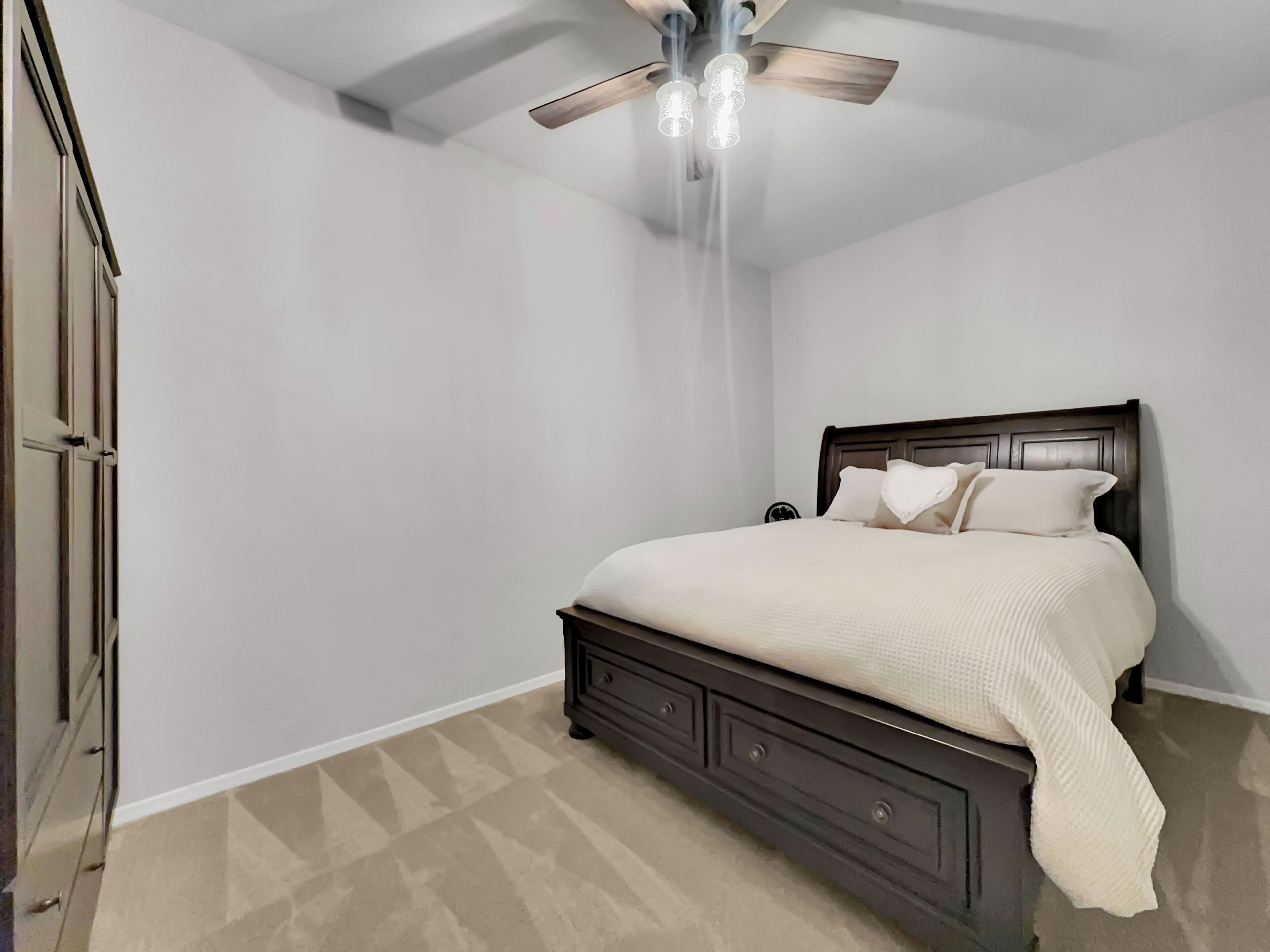 A bedroom with a bed, a nightstand, a dresser, and a ceiling fan.