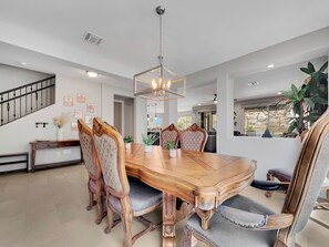 A dining area with a wooden table and chairs, a chandelier, and a staircase in the background. - 182nd Goodyear (Goodyear)