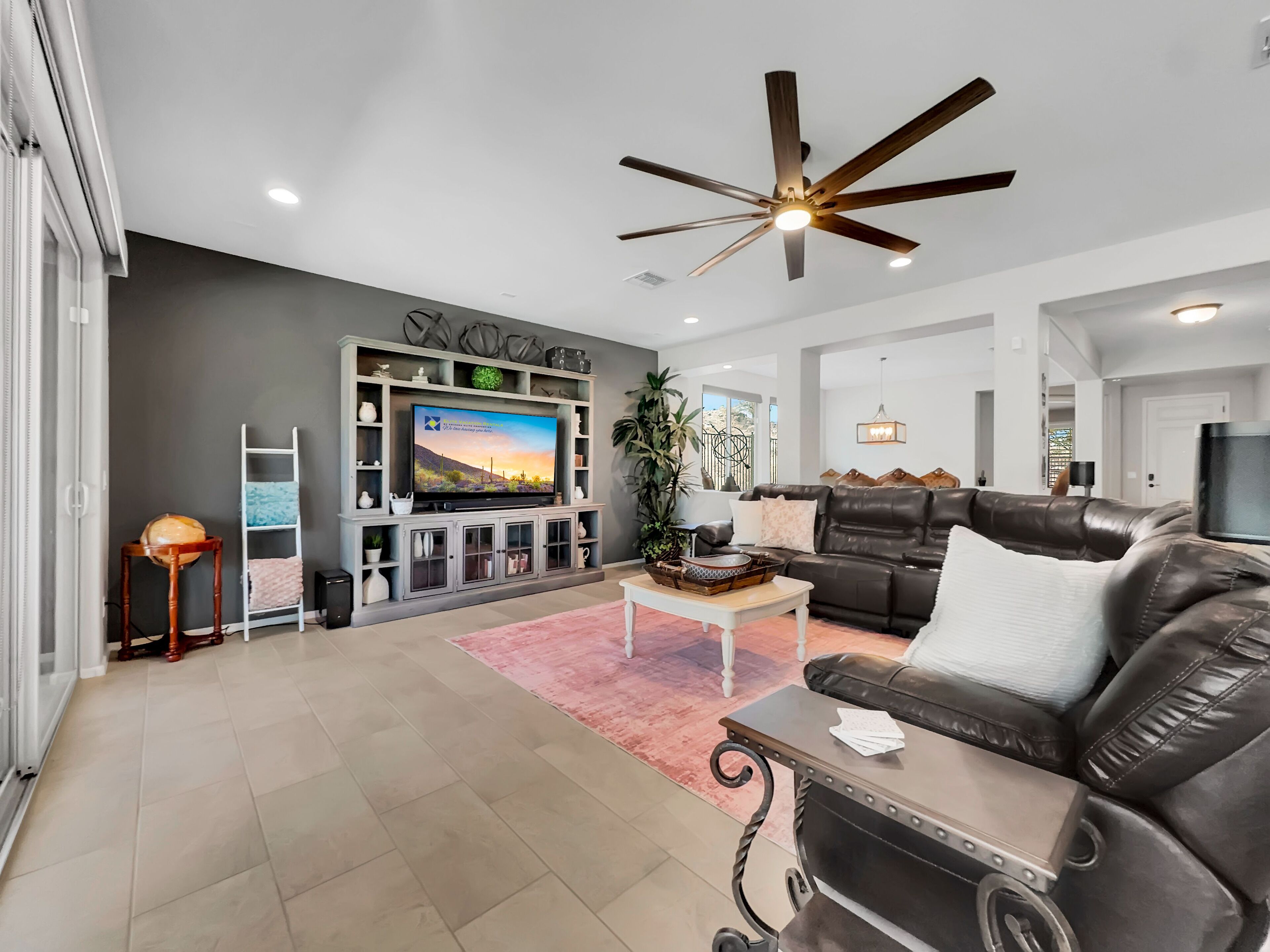 A modern living room with a flat-screen TV, leather sofa, and a ceiling fan.