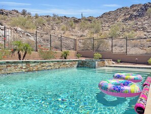 A clear swimming pool with a stone border, surrounded by a black metal fence, and a desert landscape in the background. - 182nd Goodyear (Goodyear)