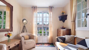 Une pièce comprenant un canapé, un fauteuil, une table en bois ornée d’un vase de fleurs, un miroir et une fenêtre avec des rideaux.