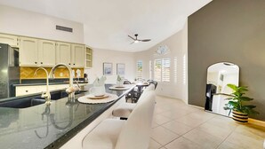 A modern kitchen with a central island, white cabinetry, and a dining area with a white chair and table. - Flame Tree Sun Lakes (Chandler)