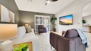 A modern living room with a white sofa, a brown armchair, a TV, and a ceiling fan. - Flame Tree Sun Lakes (Chandler)