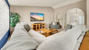A living room with a large sectional sofa, a wooden coffee table, a television, and a plant. - Flame Tree Sun Lakes (Chandler)