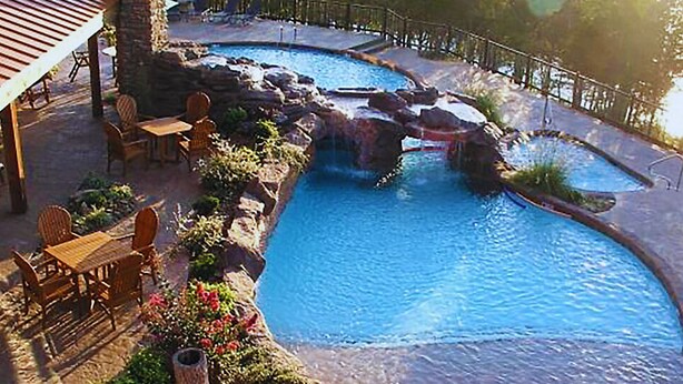 A pool with a waterfall feature, surrounded by outdoor furniture and a covered seating area. - Stonewater Cove (Shell Knob)