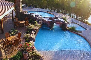 A pool with a waterfall feature, surrounded by outdoor furniture and a covered seating area. - Stonewater Cove (Shell Knob)