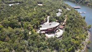 A large, two-story house surrounded by dense forest, with a dock extending into a lake. - Stonewater Cove (Shell Knob)