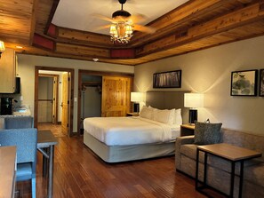 A hotel room with a large bed, a desk, a chair, a small table, a ceiling fan, and wooden walls. - Stonewater Cove (Shell Knob)