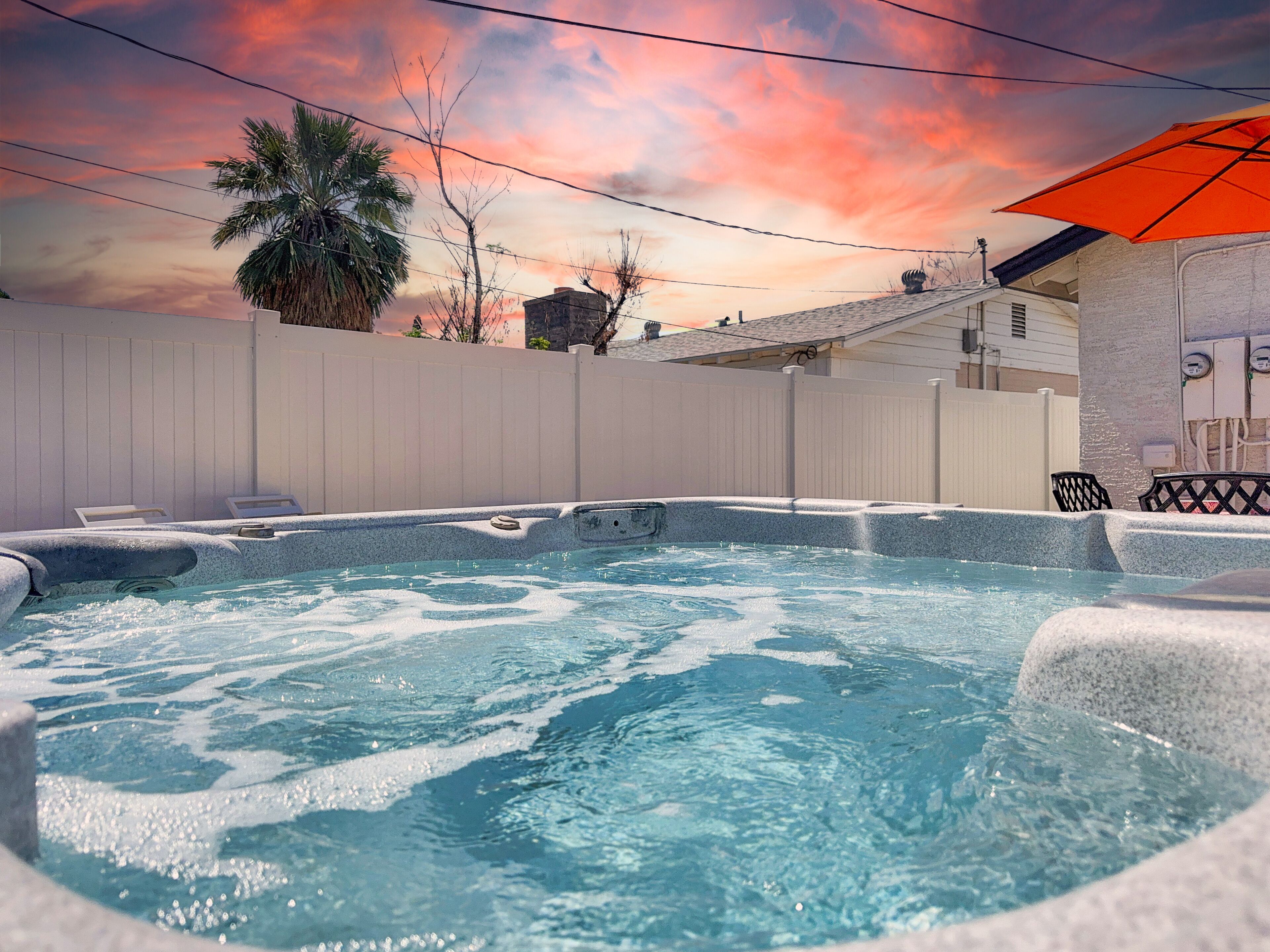 A hot tub with a white fence and a sunset in the background.