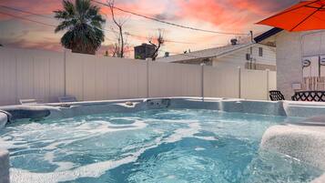 A hot tub with a white fence and a sunset in the background.