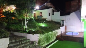 A nighttime view of a building with a staircase leading to a green lawn area, a small pool, and a well-lit garden. - Hotel Villa del Sol (Villa Gesell)