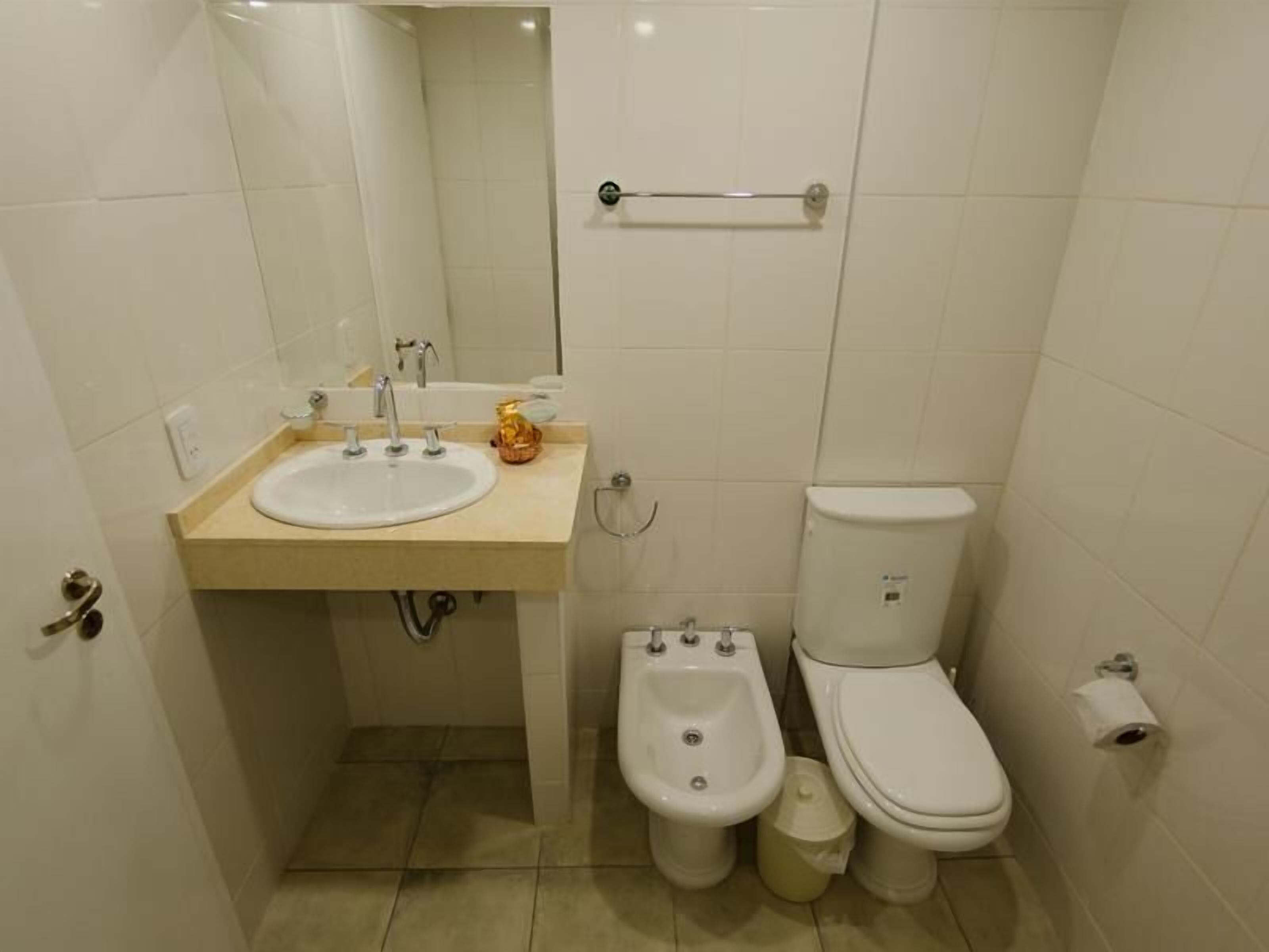 Un baño pequeño y funcional, con lavamanos blanco, inodoro y bidé.