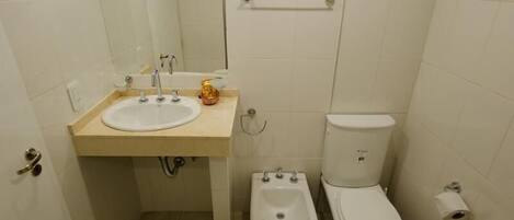 Un baño pequeño y funcional, con lavamanos blanco, inodoro y bidé.
