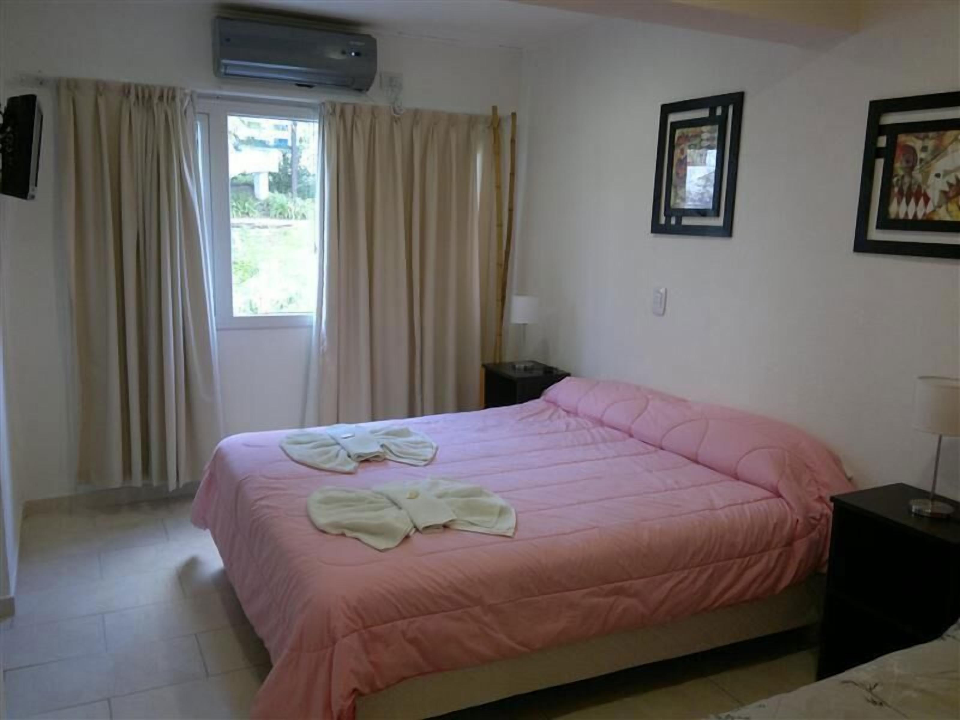 A bedroom with a bed, a nightstand, a window with curtains, and a wall-mounted air conditioner.