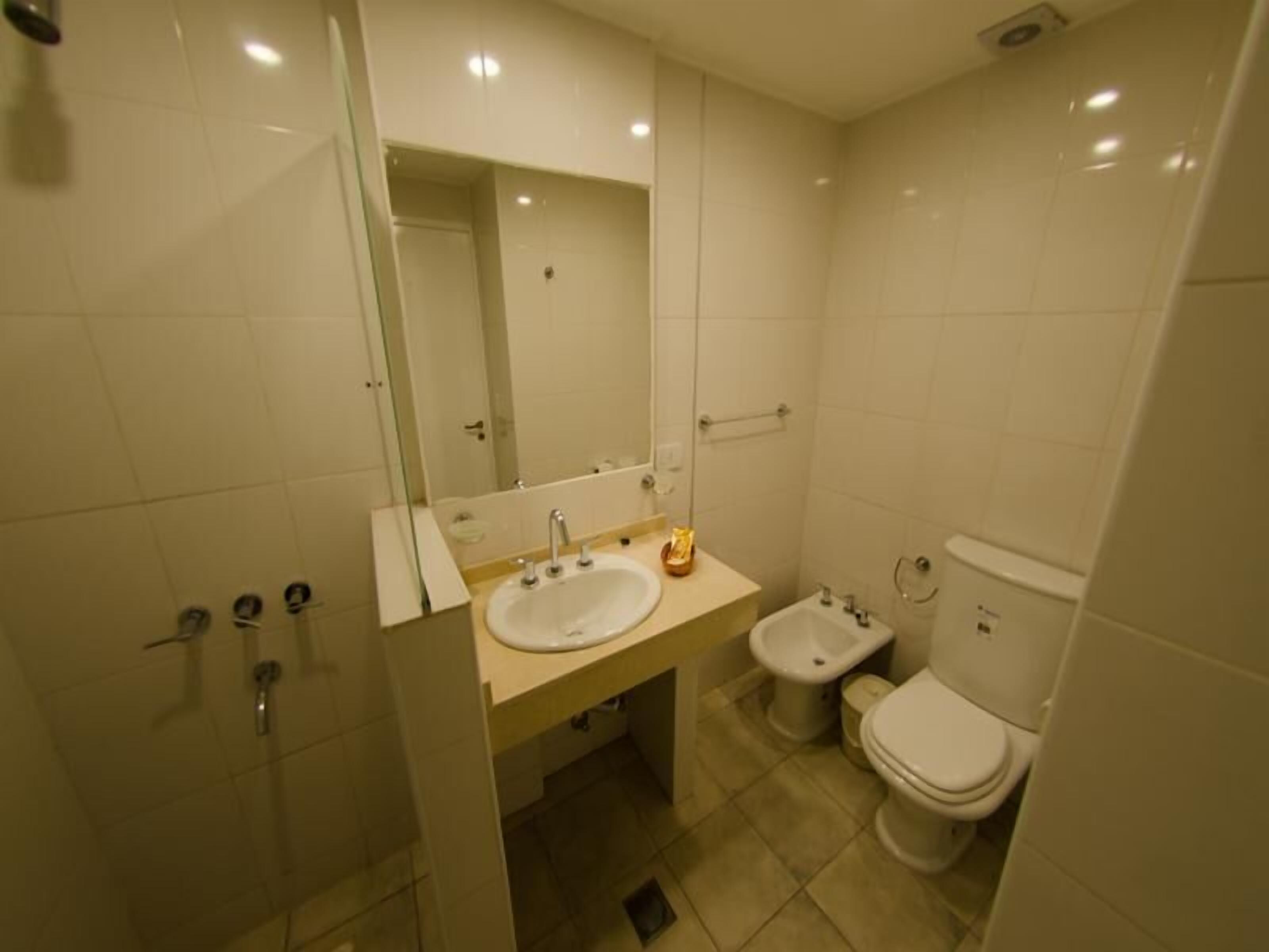 A bathroom with a sink, mirror, toilet, and bidet.