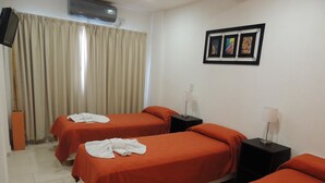 A hotel room with two beds, beige curtains, a wall-mounted air conditioner, and a framed picture above the beds. - Hotel Villa del Sol (Villa Gesell)