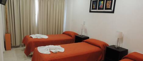 A hotel room with two beds, beige curtains, a wall-mounted air conditioner, and a framed picture above the beds.