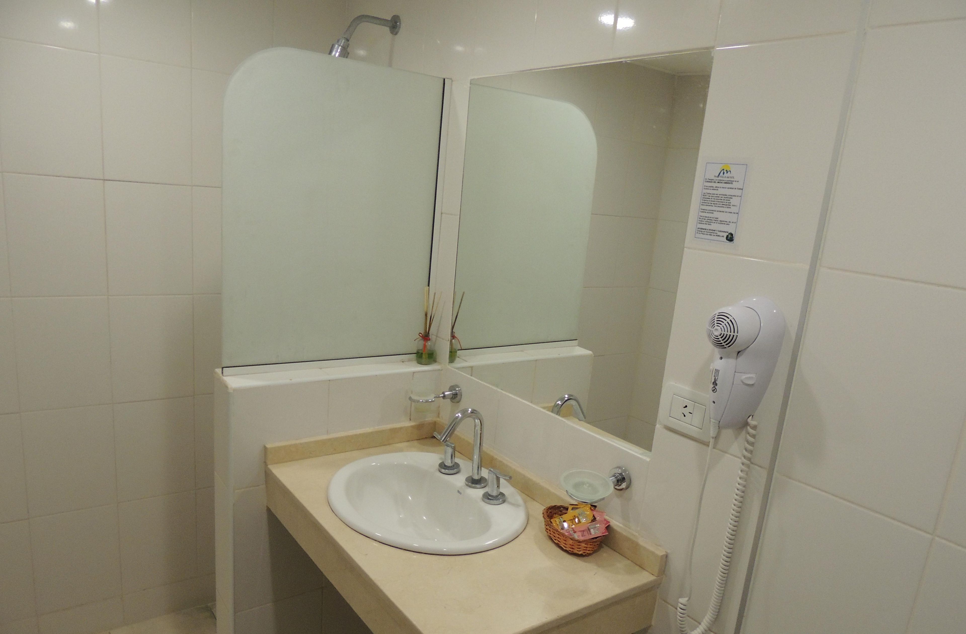 A bathroom with a sink, mirror, and a hairdryer mounted on the wall.
