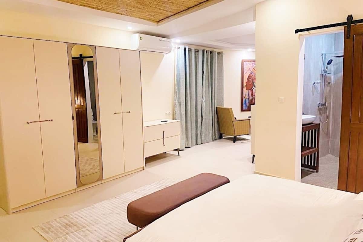 A modern bedroom with a large bed, a wardrobe, a desk, and a shower area.