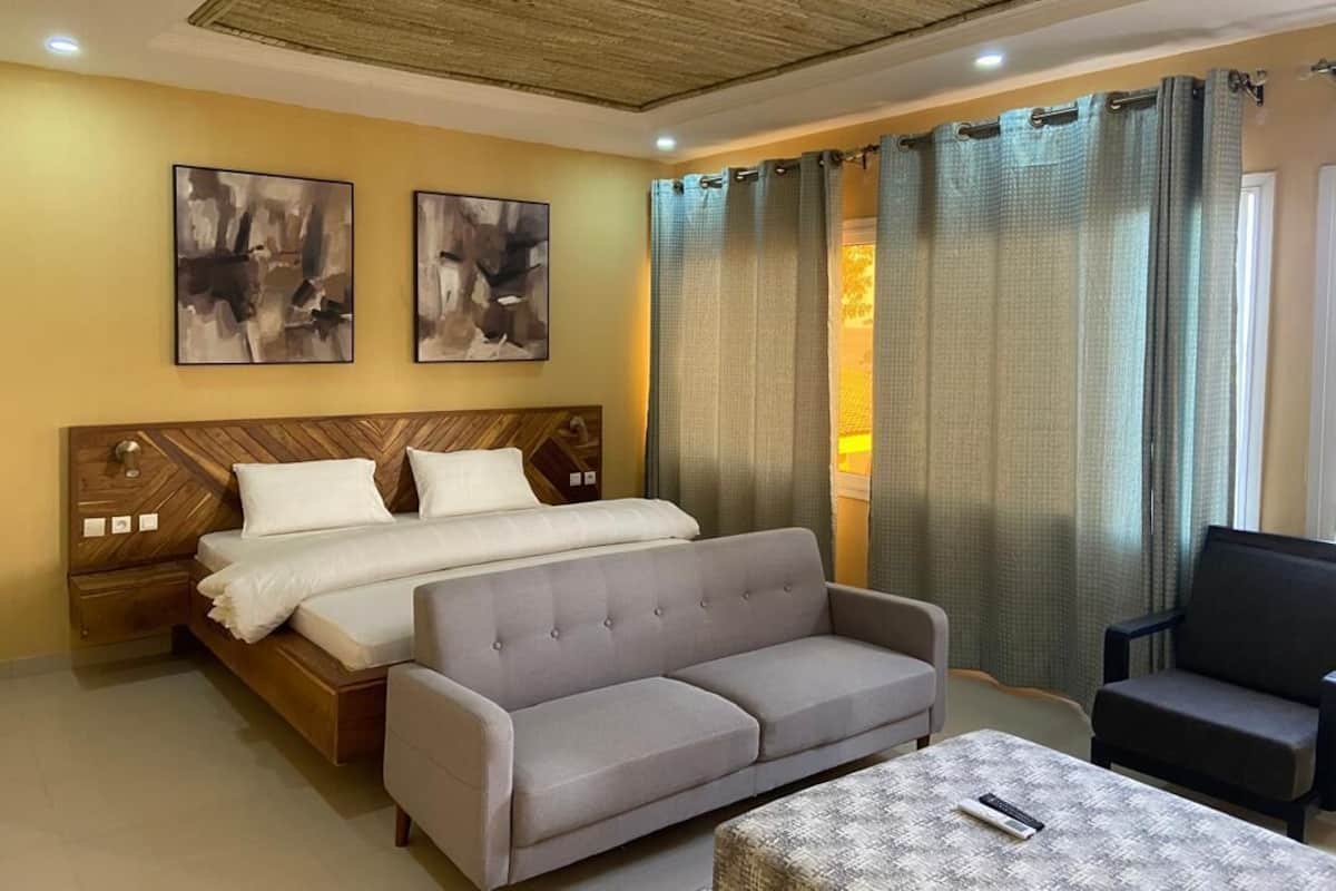 A hotel room with a bed, a sofa, a small table, and two abstract paintings on the wall.