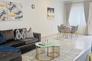 A modern living room with a sofa, coffee table, and dining area. - Fairlie Glen- Arlington Estate (Harare)