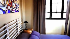 Una camera da letto con un letto, un comodino, una lampada e una finestra con tende.
