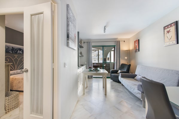Una sala de estar moderna con un sofá, una mesa de comedor y una cocina visible a través de una puerta abierta.