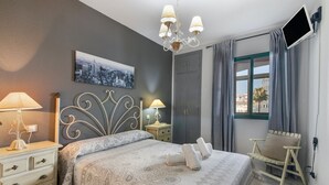 A bedroom with a bed, bedside lamps, a cityscape picture, a desk, and a chair. - Apartment 'El Portil' with Shared Pool, Wi-Fi and Air Conditioning (El Portil)