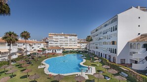 A pool area with umbrellas, lounge chairs, and a large building with multiple balconies. - Apartment 'El Portil' with Shared Pool, Wi-Fi and Air Conditioning (El Portil)