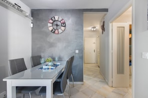 Un comedor con una mesa de vidrio, sillas, un reloj y una puerta que da a otra habitación.