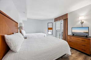 A hotel room with a large bed, a television, a wooden dresser, and a view of the ocean.