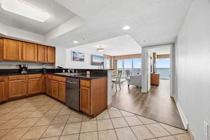 A spacious kitchen with wooden cabinets, a dishwasher, and a large island. There is a dining area with a view of the ocean. - 2BR Beachfront Boardwalk Condo (Myrtle Beach)