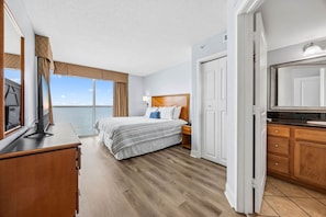 A hotel room with a large bed, a desk with a computer, a TV, and a view of the sea. - 2BR Beachfront Boardwalk Condo (Myrtle Beach)