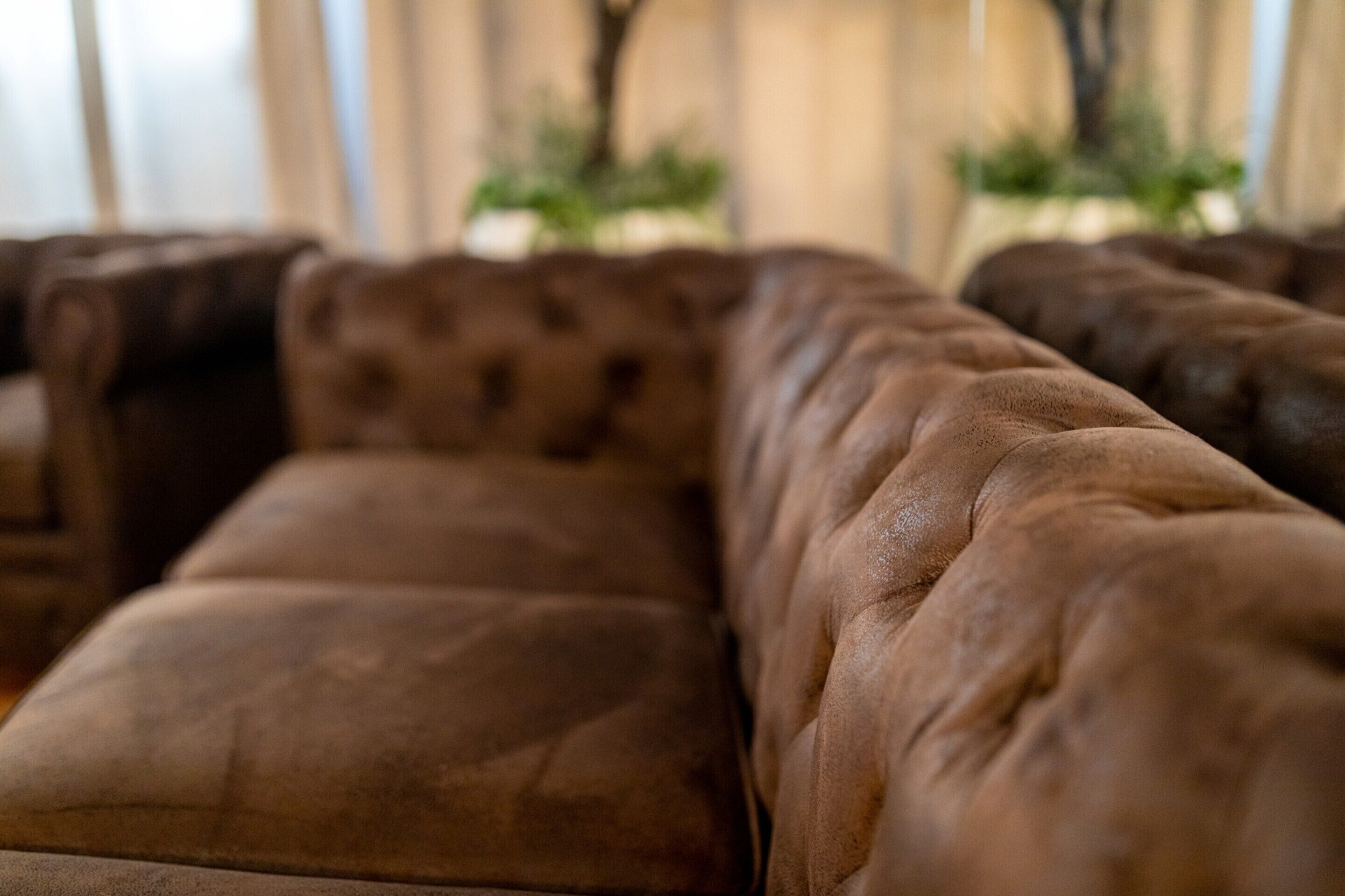 A close-up of a brown leather sofa with a tufted backrest.
