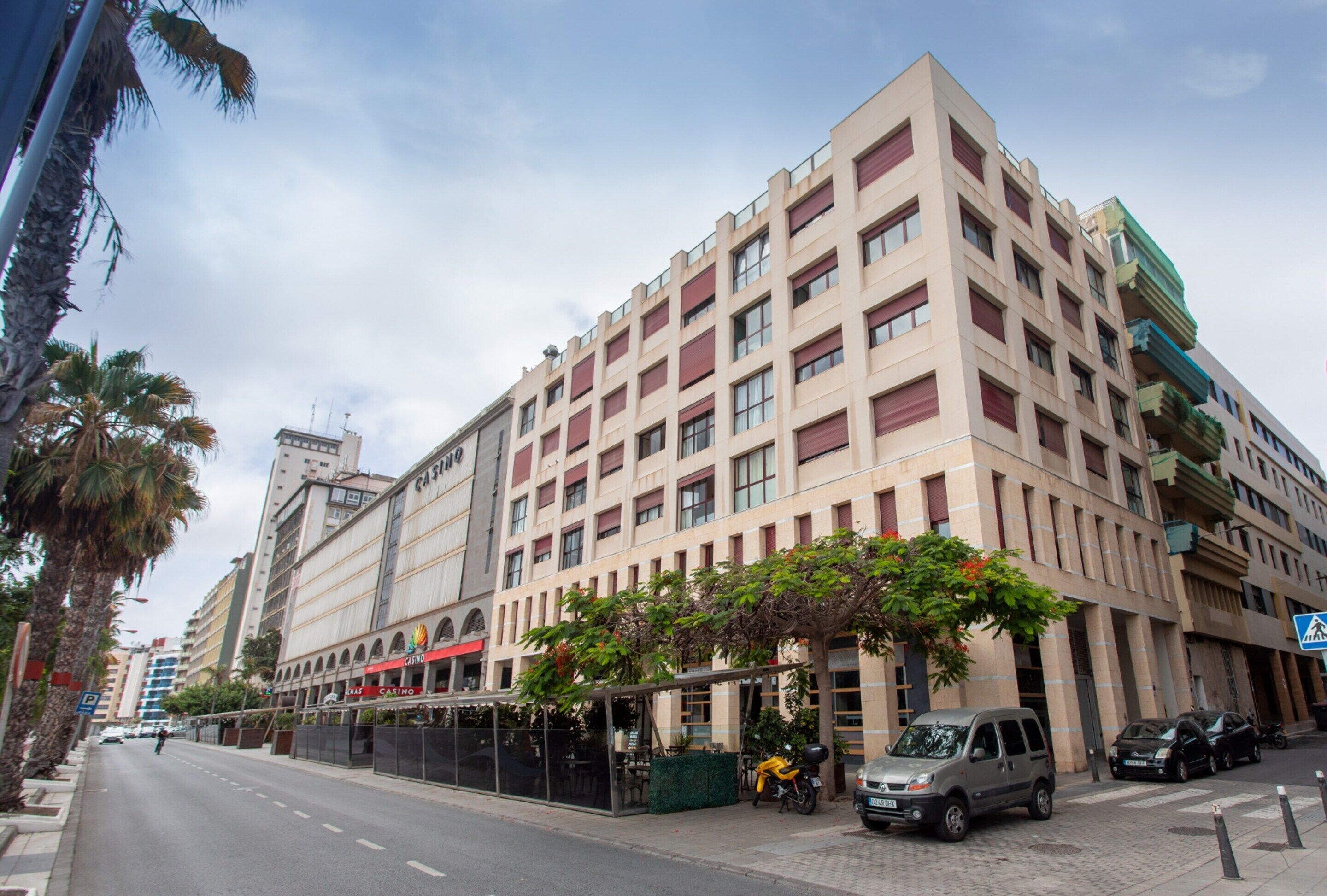 A multi-story hotel with a modern facade, a covered outdoor seating area, and a parking lot.